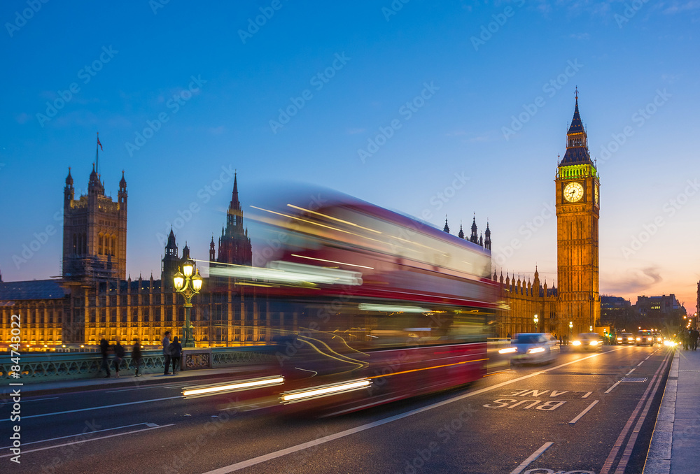 London, United Kingdom - Iconic Double Decker bus on the move on Westminster bridge with illuminated Big Ben clock tower and Parliament at background at blue hour