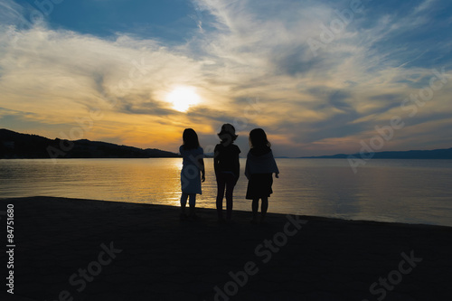 Three little girls watching the sunset against a dramatic sky.