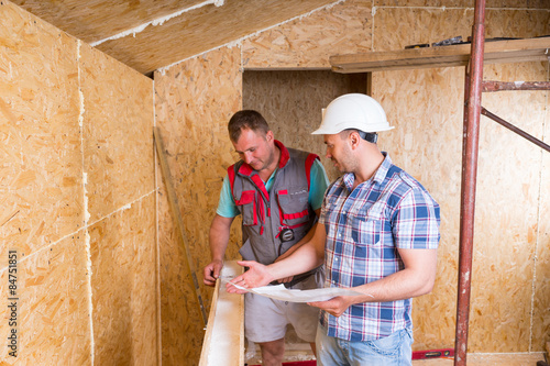 Slika na platnu Foreman with Plans Monitoring Worker In New Home