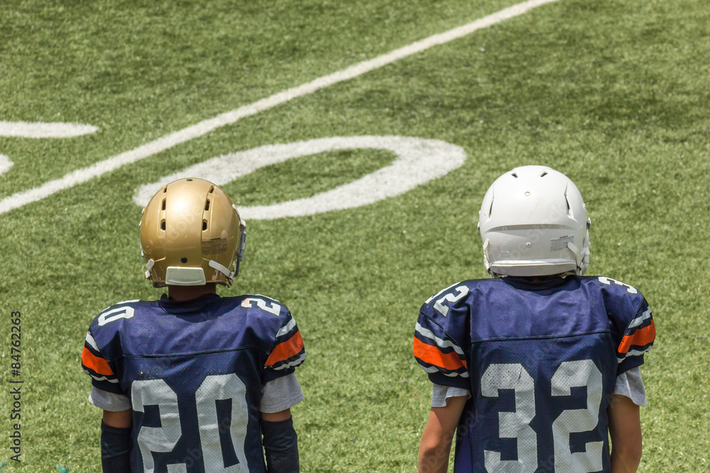 Kids standing back on a football field with helmets and blue jerseys Kids standing back on a football field with helmets and blue jerseys