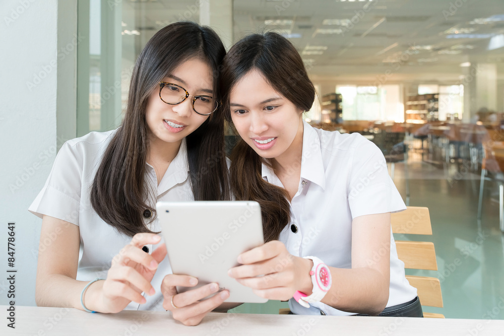 Two Asian student with uniform in classroom with electronic tabl Two Asian student with uniform in classroom with electronic tabl