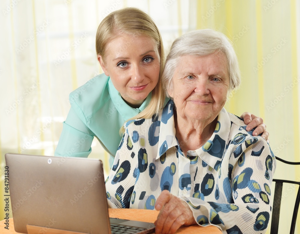 Senior woman with her caregiver in home using laptop.