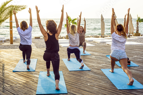 Photo group of young females practicing yoga on the seaside during the sunrisе
