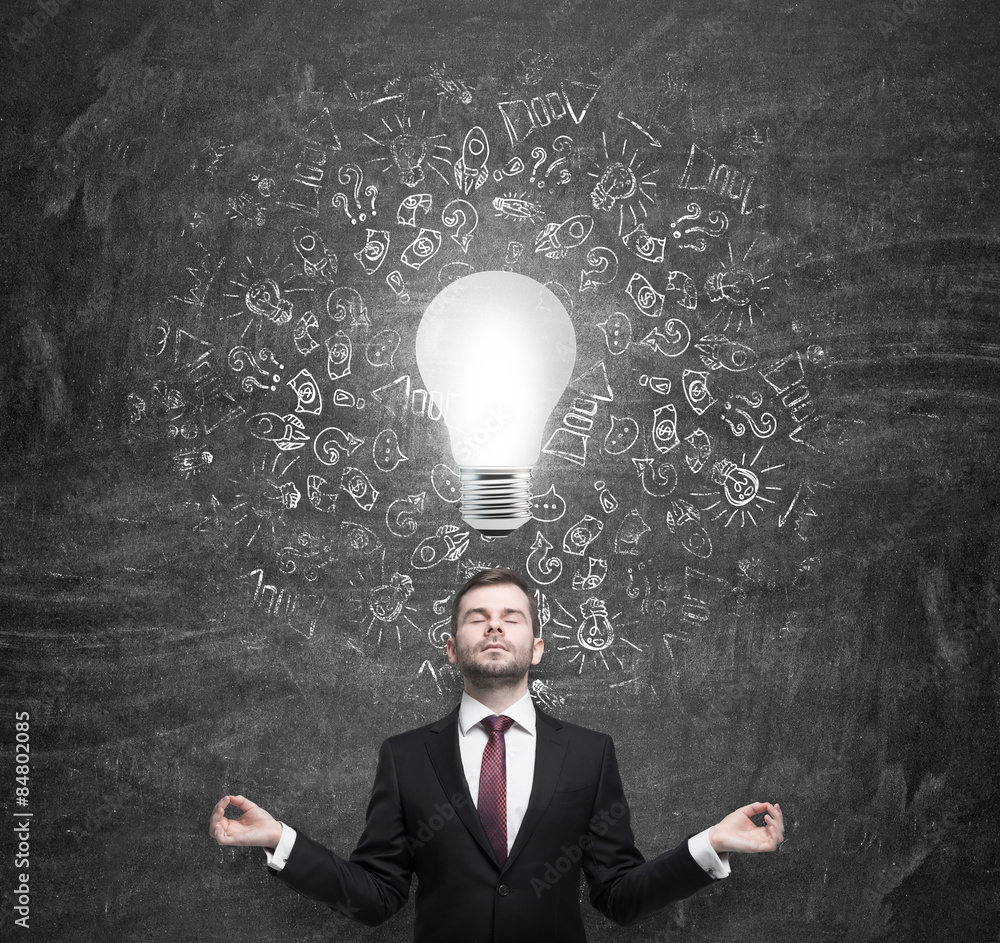 Meditating young businessman thinking about the light bulb. A concept of the brainstorm in business development. Meditating young businessman thinking about the light bulb. A concept of the brainstorm in business development.