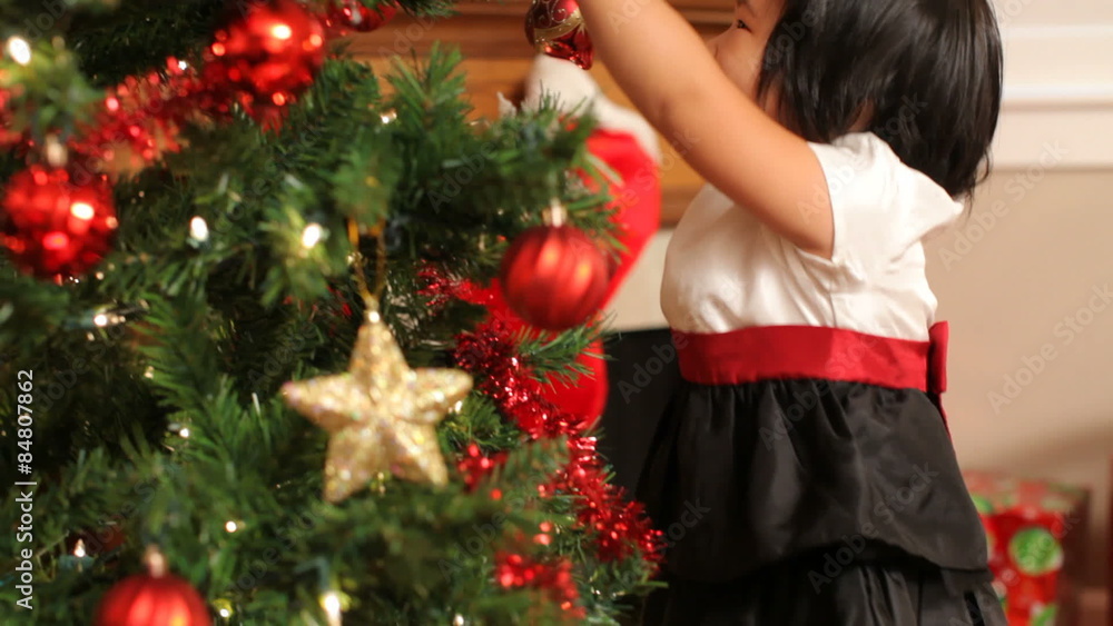 Young girl putting ornament on Christmas tree Young girl putting ornament on Christmas tree