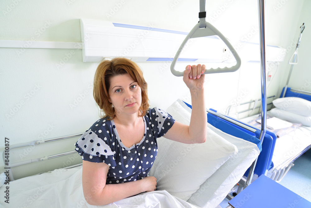 Female patient holding on to device for lifting in hospital room Female patient holding on to device for lifting in hospital room