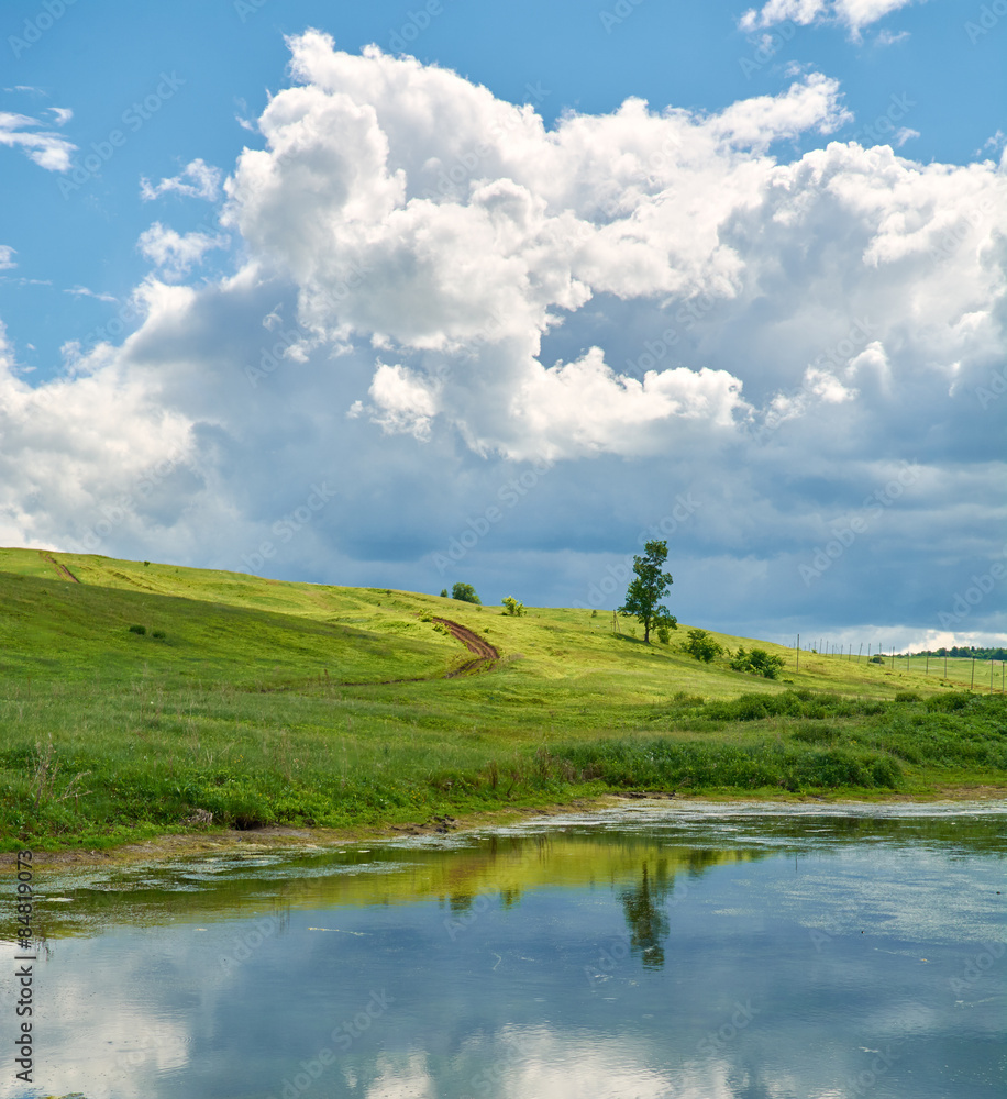 Obraz premium Reflection of the sky with clouds in the water near the green hill