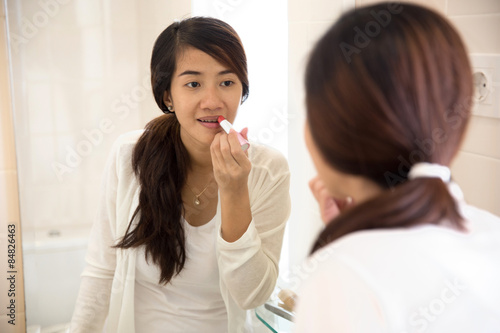 Beautiful asian woman putting make-up on, applying lipstick on h