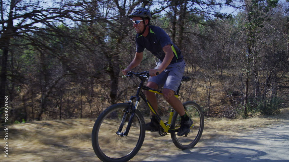 Man riding mountain bike down gravel road, tracking shot Man riding mountain bike down gravel road, tracking shot