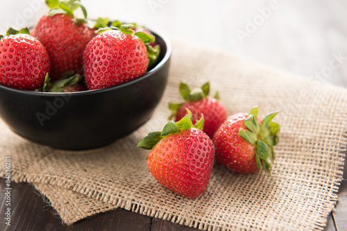 Fresh strawberries in a bowl on wooden background.