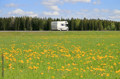 White Motorhome on Spring Road with Yellow Flowers and Copy Space