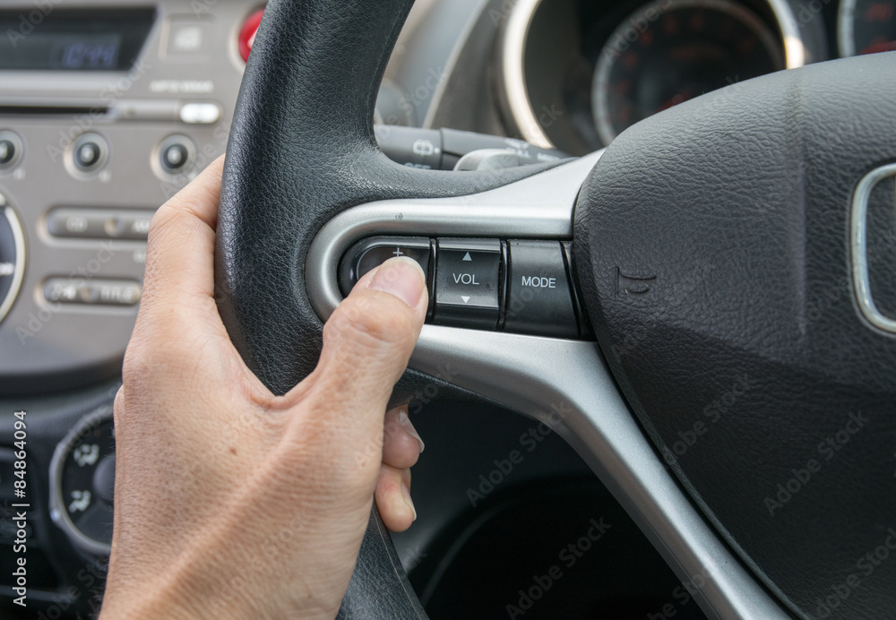 A hand pushes the cruise control button on a steering wheel. A hand pushes the cruise control button on a steering wheel.