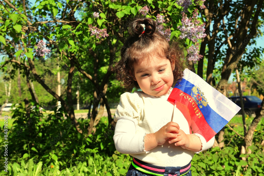 Small girl stands with flag of Russia in front of lilac Bush on sunny day Small girl stands with flag of Russia in front of lilac Bush on sunny day