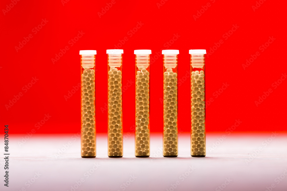 five small glass tubes with homeopathy globules, red background