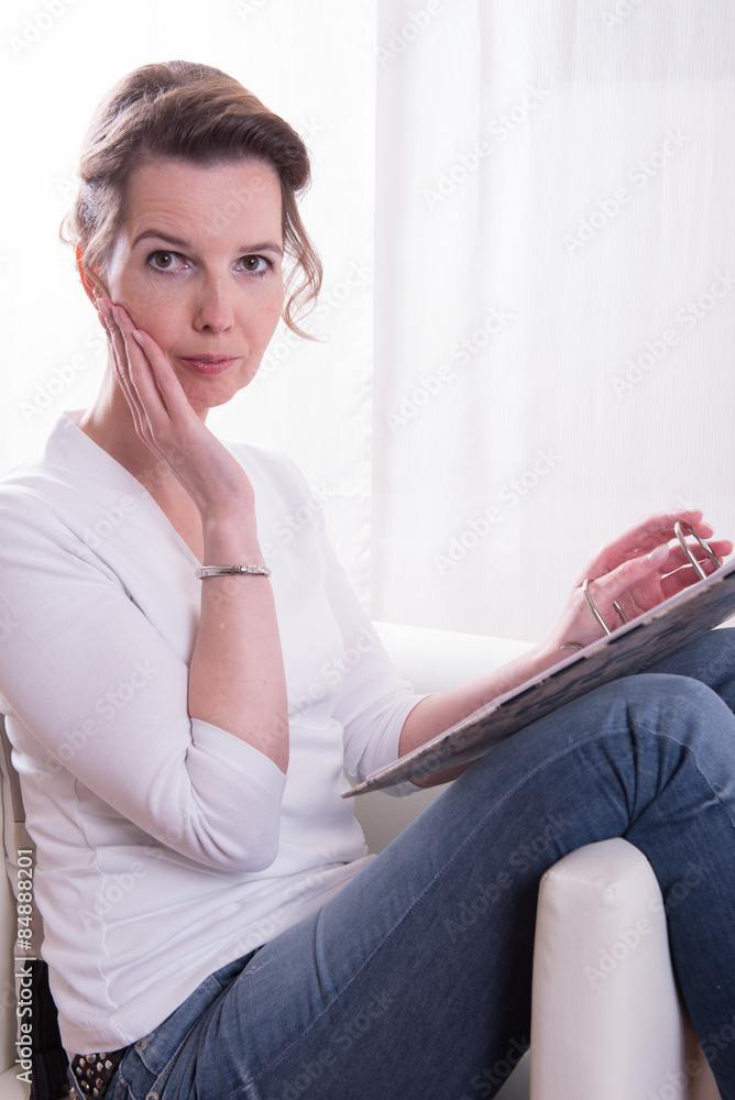 Frau sitzt im Sessel und arbeitet an einem Ordner Frau sitzt im Sessel und arbeitet an einem Ordner