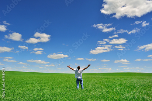 man with arms raised on a green field under beautiful sky