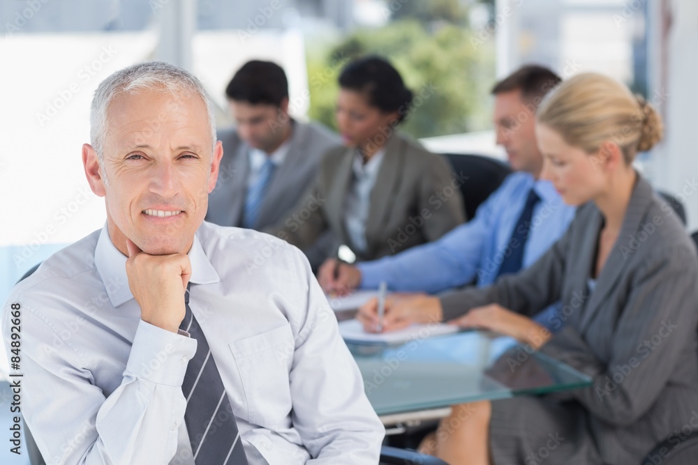 Businessman smiling at camera with colleagues behind Businessman smiling at camera with colleagues behind