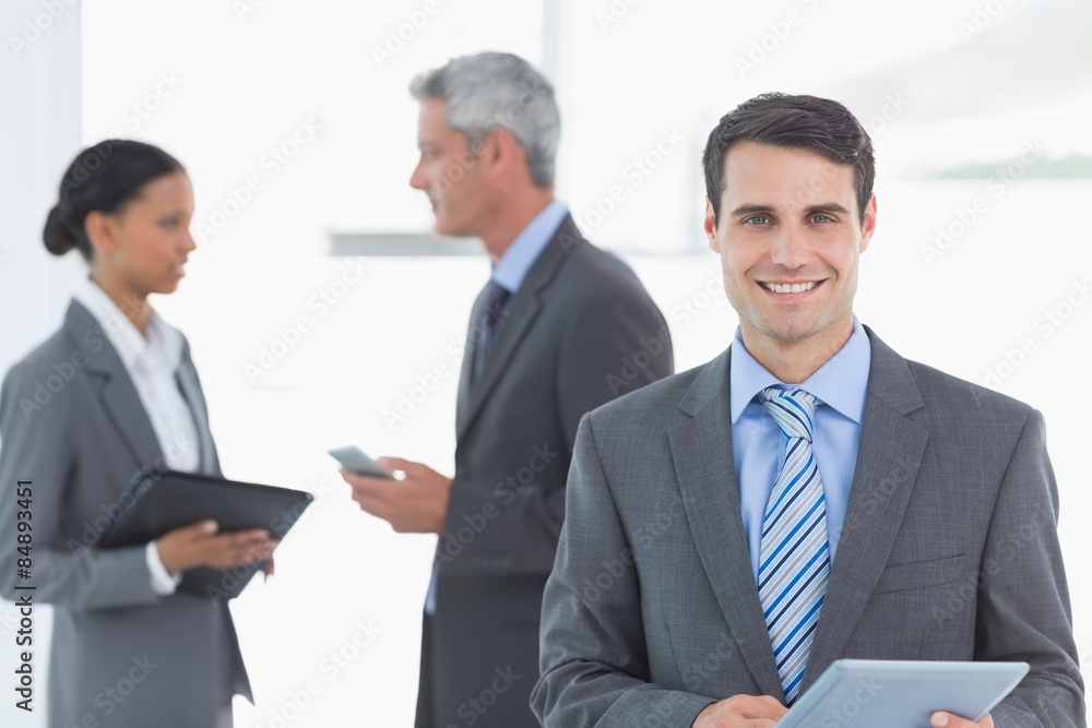 Businessman using a tablet with colleagues behind in office Businessman using a tablet with colleagues behind in office