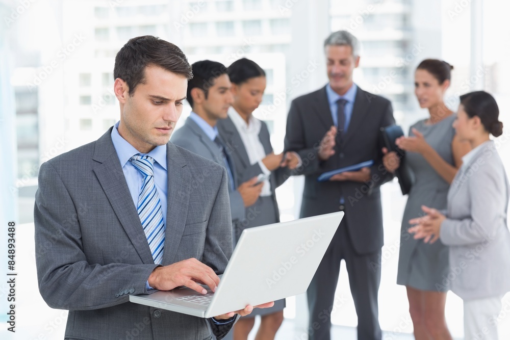 Businessman using laptop with colleagues behind Businessman using laptop with colleagues behind