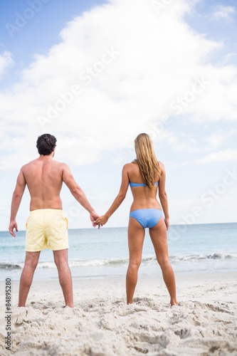 Happy couple holding hands and looking at the sea 