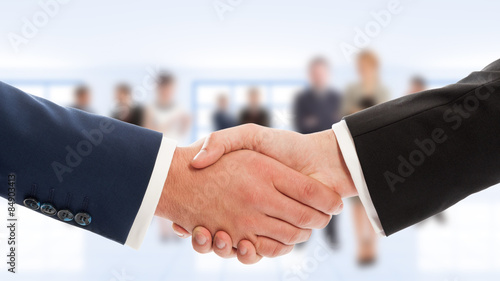 Businessmen hand shake with business people in background