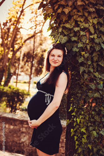 pregnant woman stands next to the sunset in the garden