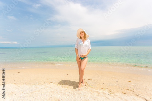 woman in white shirt and hat posing on sandy beach at sunny day
