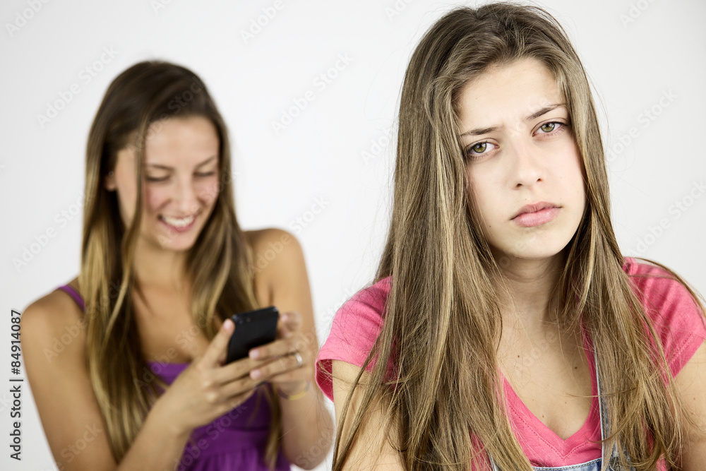 Female teenager very sad while girlfriend is laughing with cell phone Female teenager very sad while girlfriend is laughing with cell phone