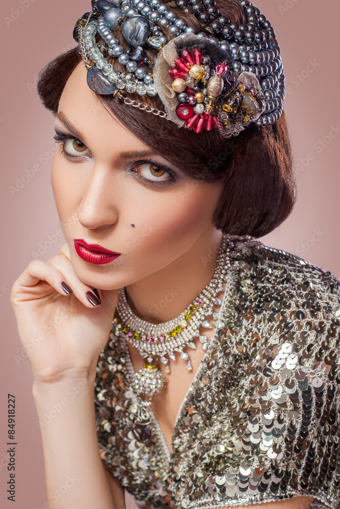 Retro styled fashion portrait of a young woman with pearls. Clothing and makeup in vintage silver style, looking at camera with passion. 
