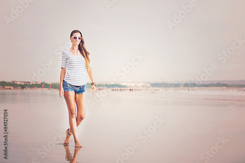 Beautifil young woman walking along the beach at sunset enjoing