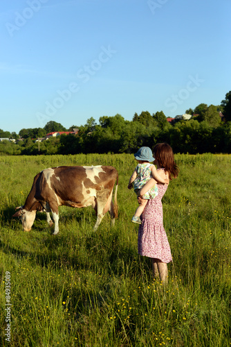 Young mother with her baby daughter watching a cow grazing