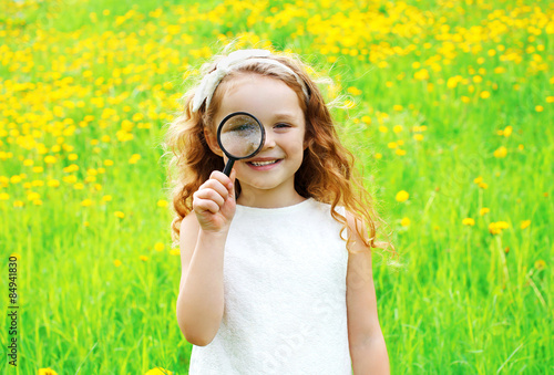 Portrait of positive little girl looking through a magnifying gl