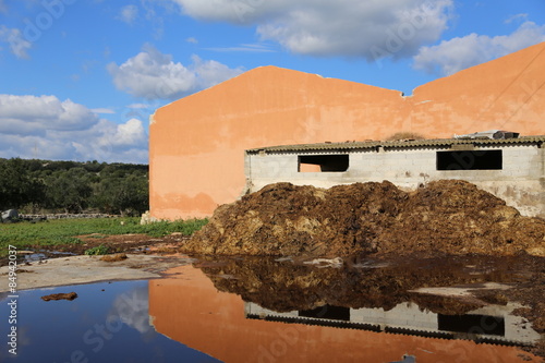 Modica, IT, January 24, 2015: pile of manure in a Sicilian countryside. The mirror effect due to the presence of a puddle of water gives the photograph a particularly fascinating.