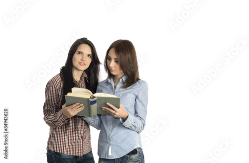 Young women read book on white background. Image of two girls dressed in checkered red blue striped brown shirts jeans casual style keeping large old book and reading it expressing bright emotions