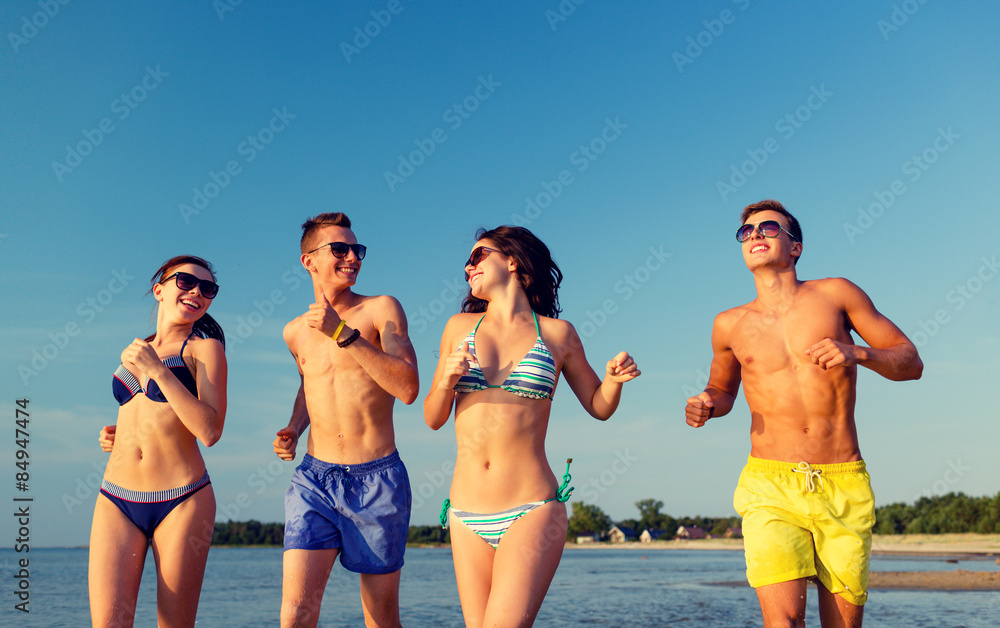 smiling friends in sunglasses running on beach