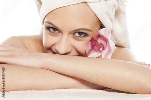 smiling woman with orchid and towel on her head lying on white
