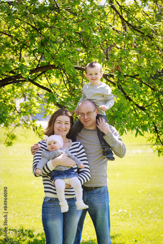 Portrait of mother, father, daughter and son, happy family of four, sitting on the meadow in the park outside on a spring summer bright day Portrait of mother, father, daughter and son, happy family of four, sitting on the meadow in the park outside on a spring summer bright day
