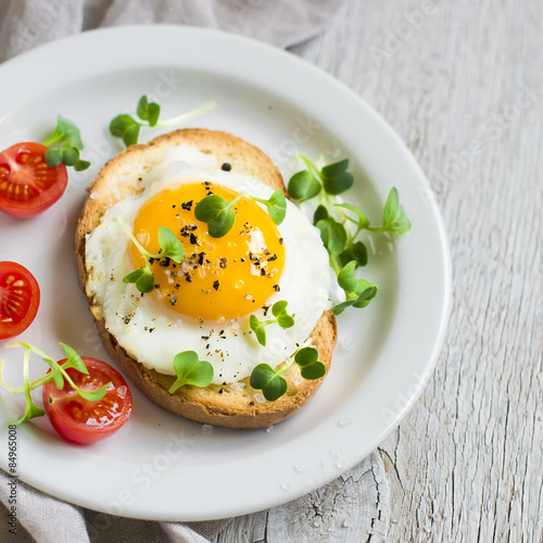 toast with fried egg and tomatoes on a light wooden background