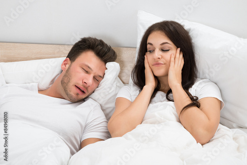 Woman Covering Ears While Man Snoring On Bed