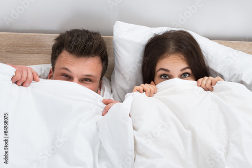 Young Couple Peeking From Bedsheets