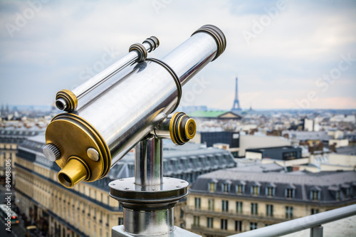 Chrome telescope on the terrace of Lafayette galleries over Paris cityscape on background