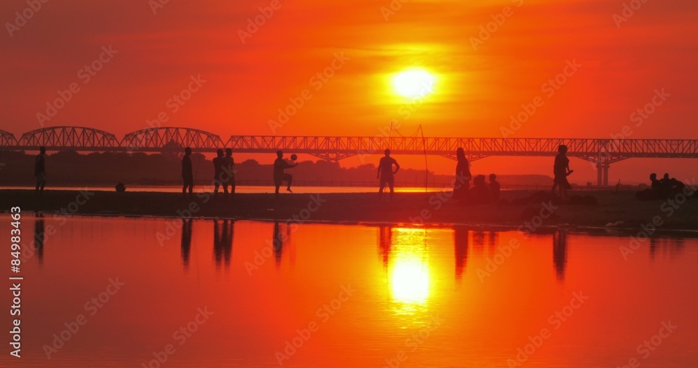 Local Burmese people play football on river bank at sunset Local Burmese people play football on river bank at sunset