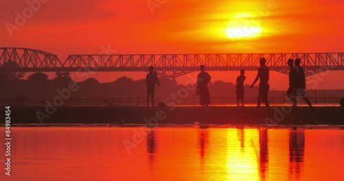 Silhouettes of people playing soccer on shore of Irrawaddy river and red sunset photo