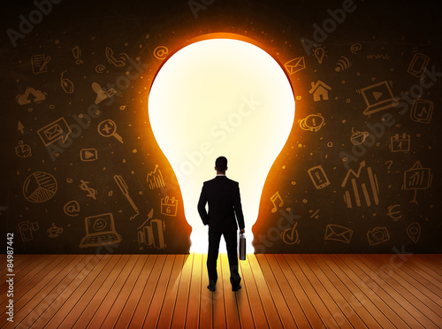 Business man looking at bright light bulb in the wall