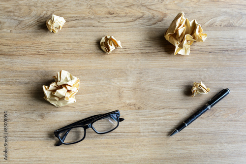 Crumpled paper balls with eye glasses and pen on wood desk