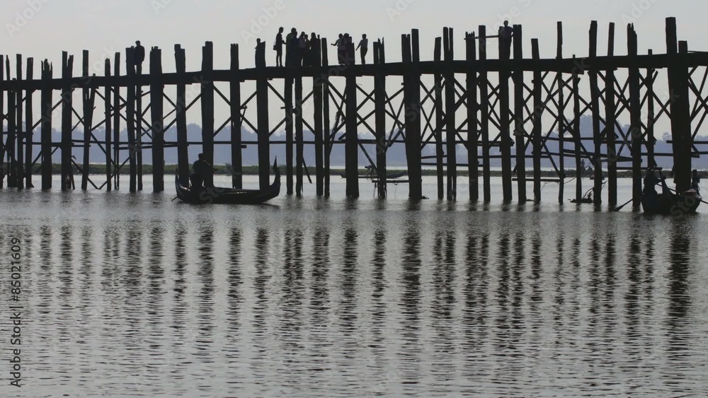 Silhouettes of people and pillars of U Bein bridge reflect in water of lake Silhouettes of people and pillars of U Bein bridge reflect in water of lake