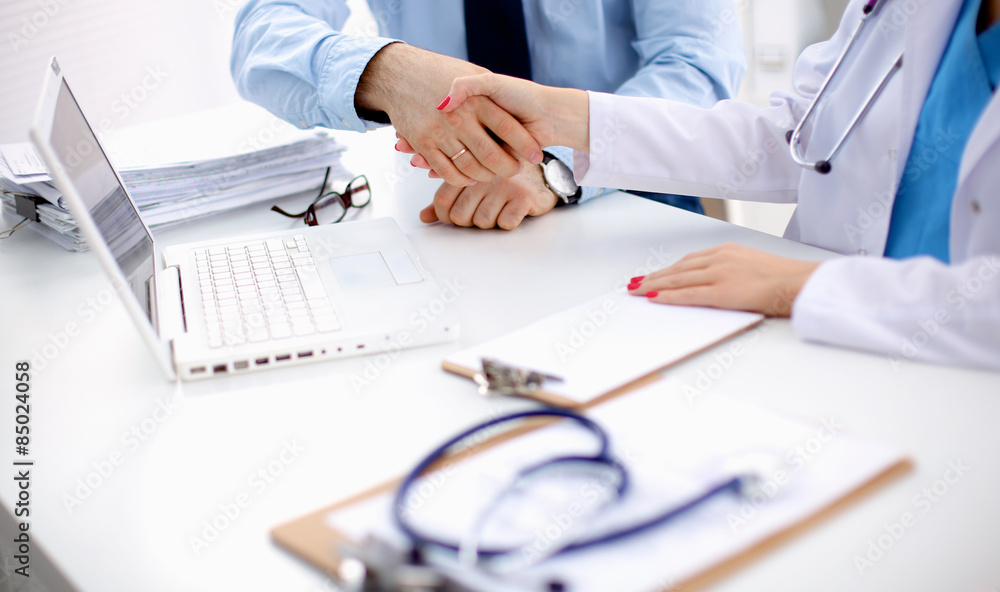 Attractive female doctor shaking a patient's hands in her office Attractive female doctor shaking a patient's hands in her office