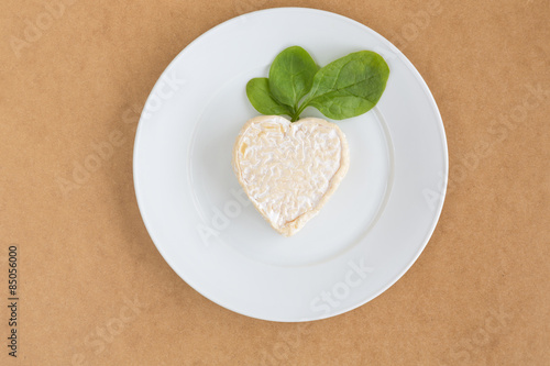 сыр с листьями салата шпинат на белой тарелке сверху на бежевом фоне