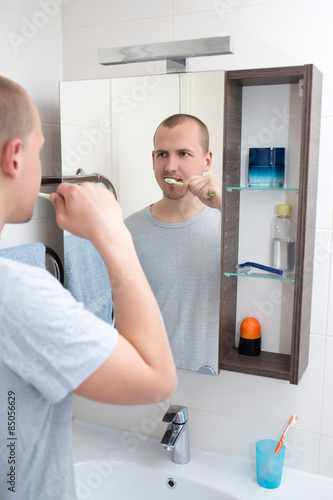 handsome man brushing teeth and looking at mirror in bathroom