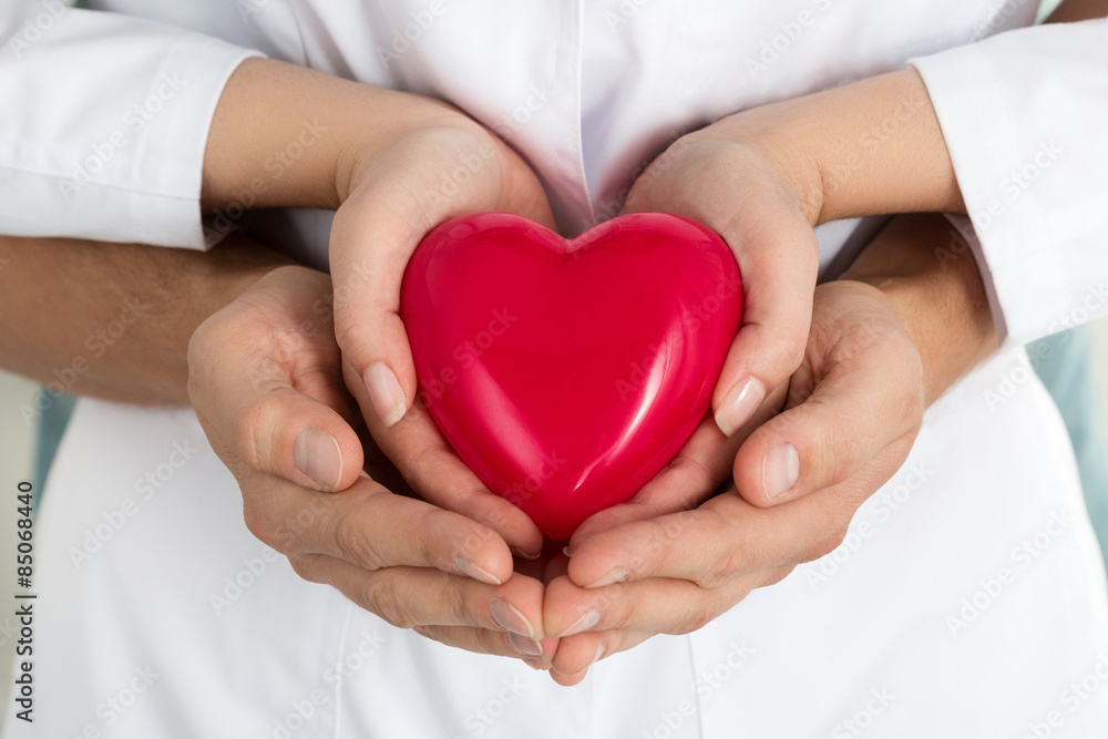 Woman's and man's hands holding red heart together Woman's and man's hands holding red heart together